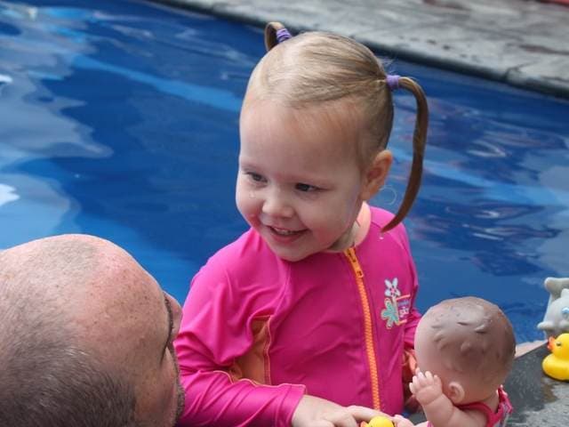 A toddler playing with water toys at the pool edge during a lesson
