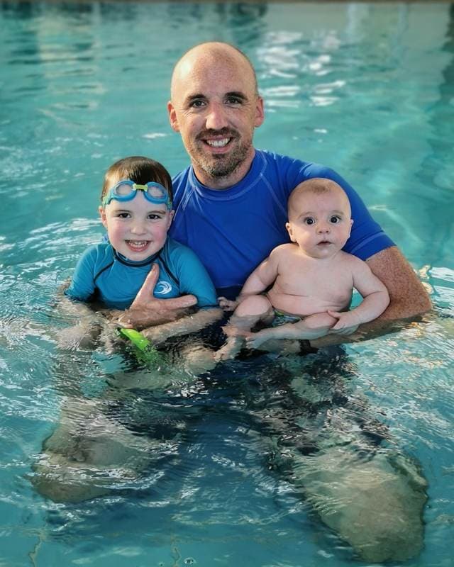 A smiling swim teacher in the pool with two young students